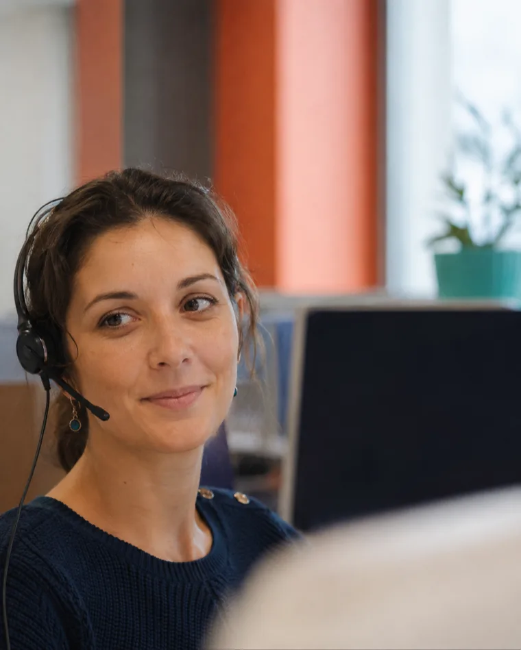 Portrait authentique d'une conseillère clientèle COMEARTH souriante à son poste de travail